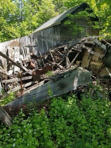 An old house is sitting in the middle of a forest surrounded by trees.