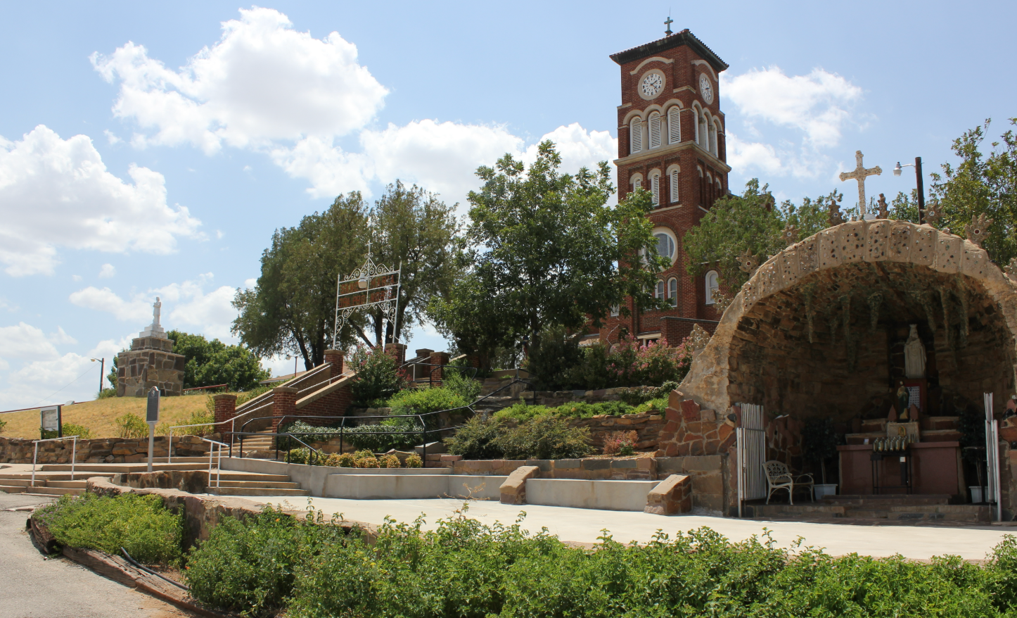 Brick clock tower and grotto on a landscaped hill with blue sky.