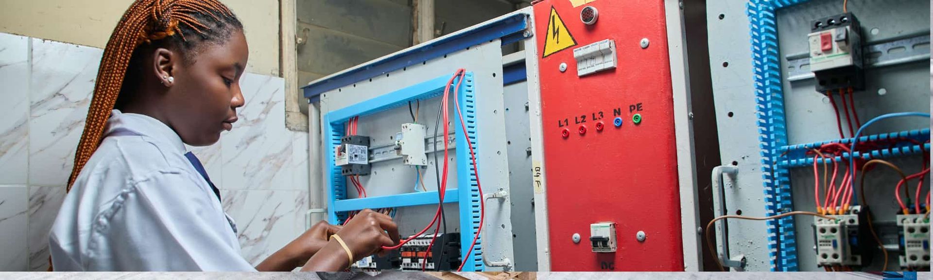 Technician working at a control panel beside industrial electrical equipment and wiring