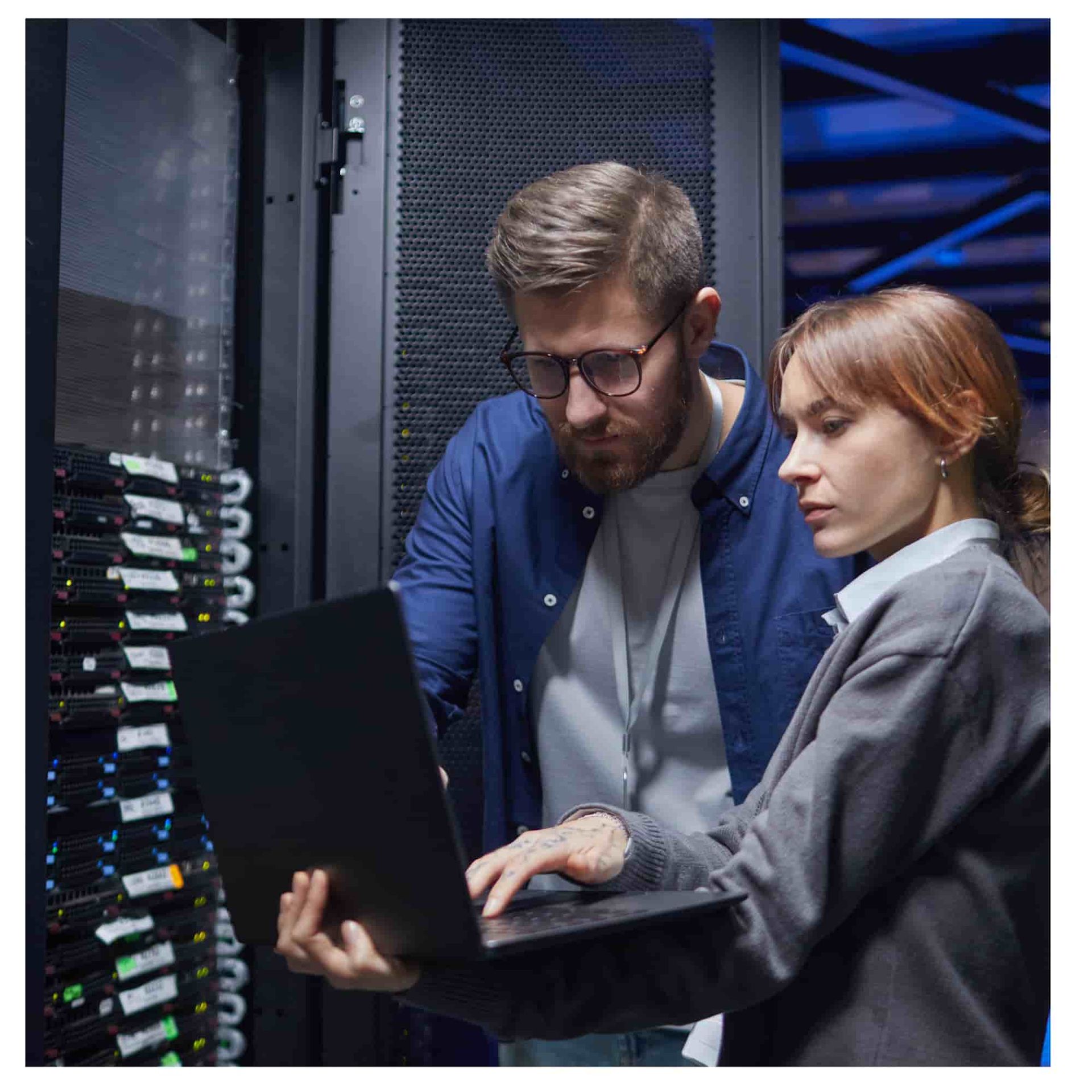 Two technicians examining a laptop in a server room with glowing network racks
