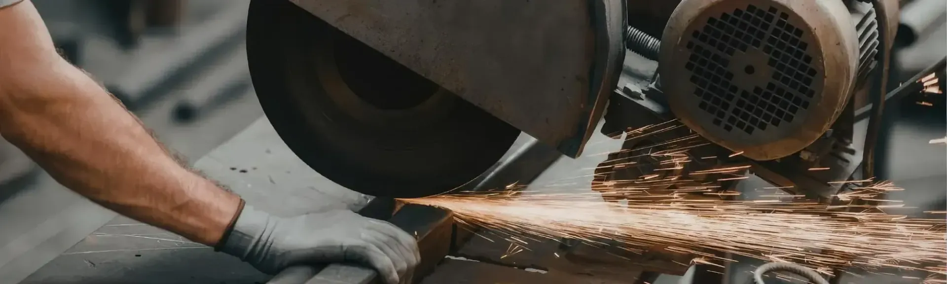 Worker cutting metal with an angle grinder, sending bright sparks across a workshop floor