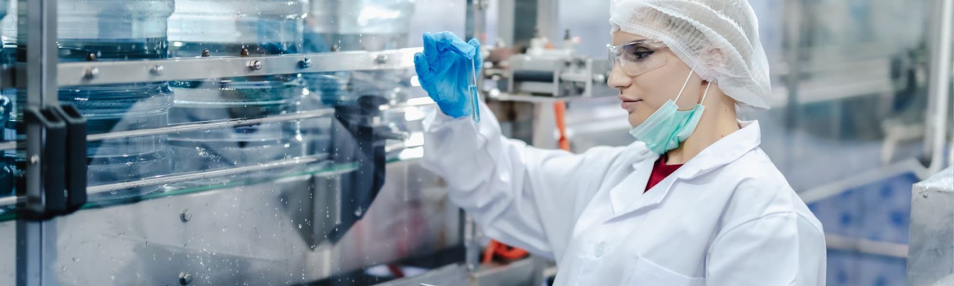 Scientist in lab coat and hairnet handling blue samples in a modern laboratory
