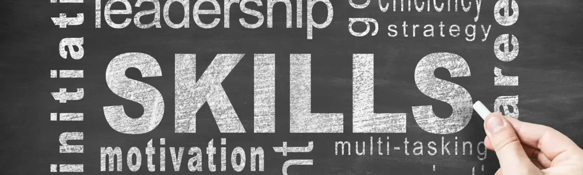 A hand writes with chalk on a blackboard displaying the word