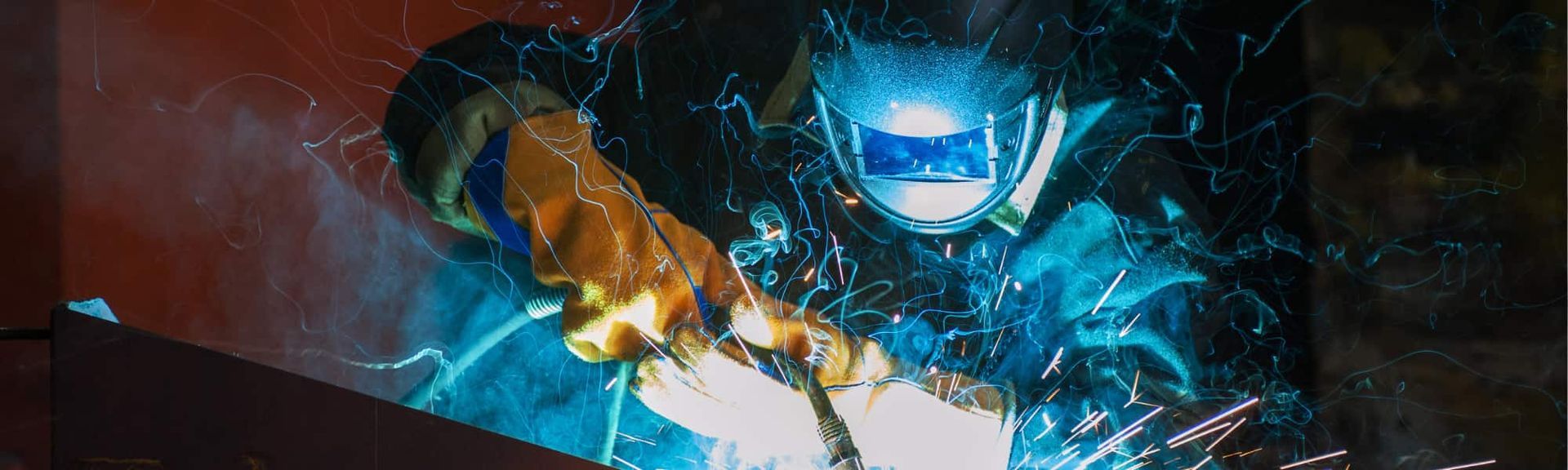 A welder reaching forward through sparks and swirling energy in a dark scene