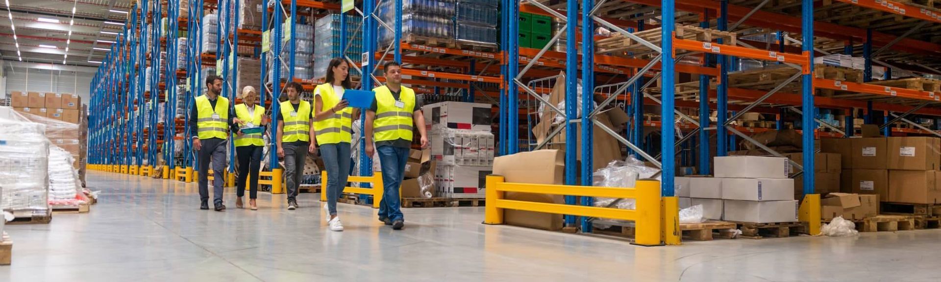 A group of warehouse employees in high-visibility vests walking and discussing work in a large, modern logistics facility.