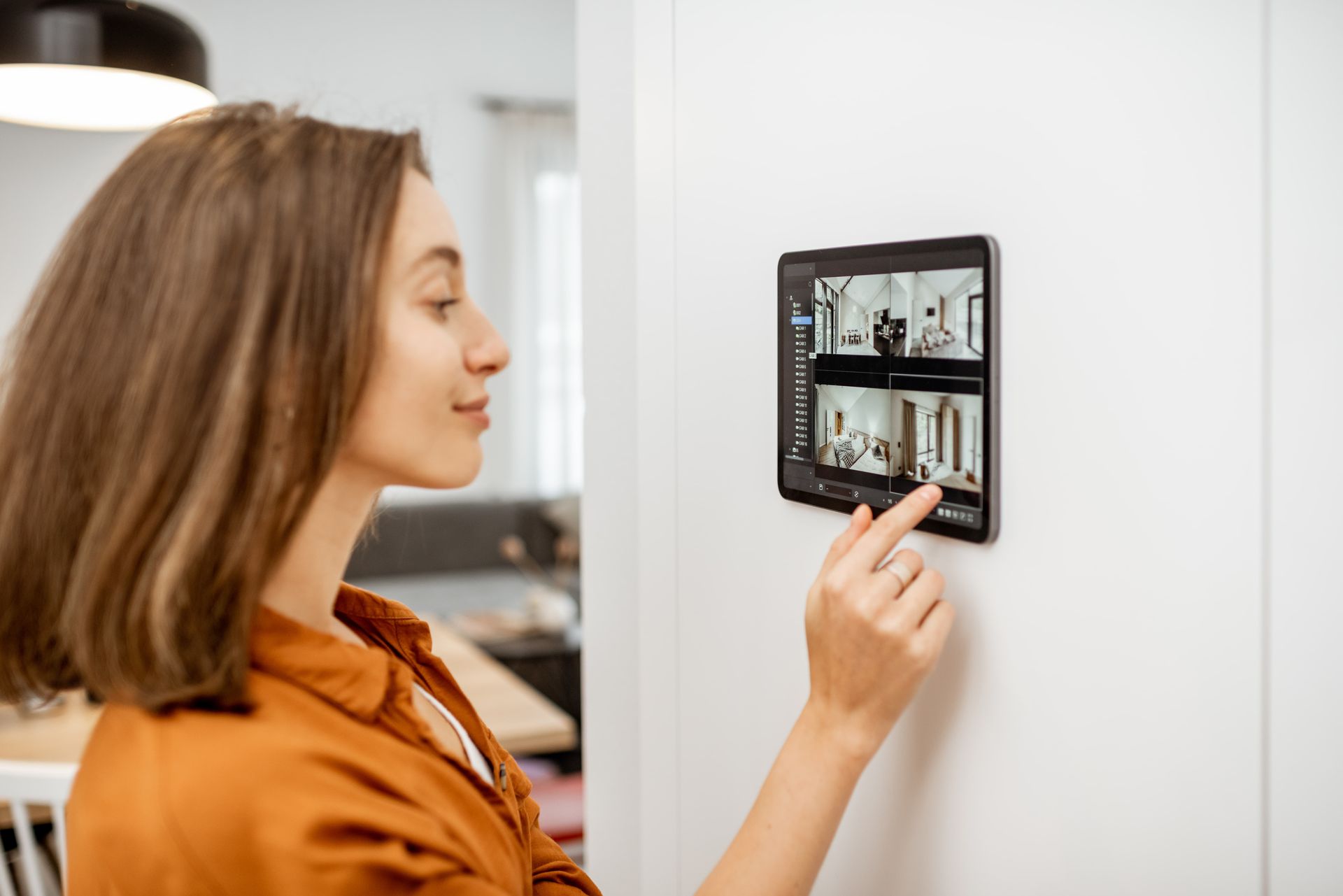 Woman using a wall-mounted touchscreen home control panel in a modern room.