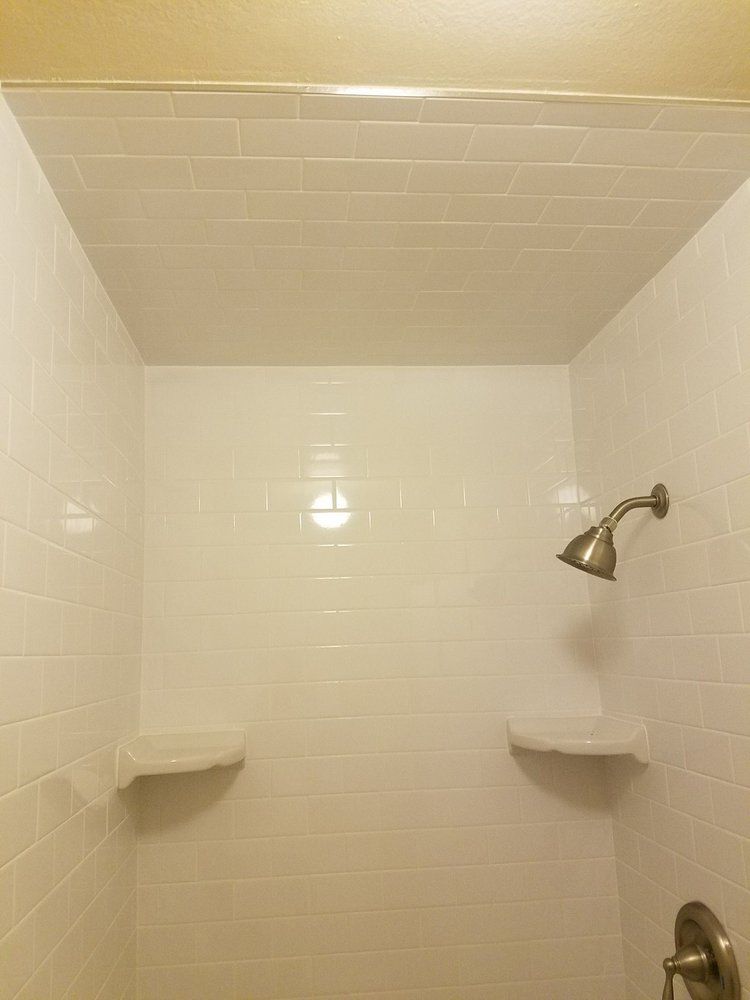 A bathroom with white tile walls and a shower head.