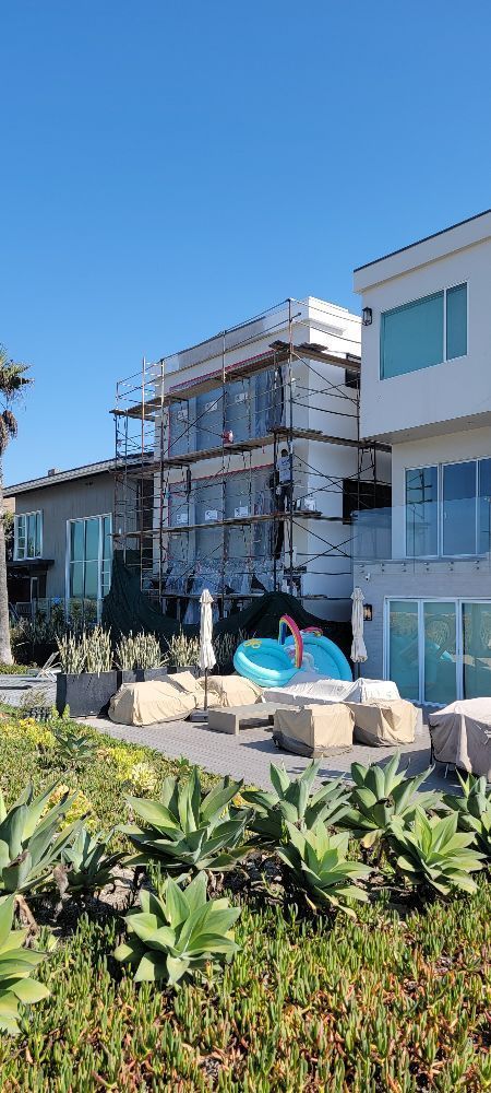 A large white house with scaffolding around it is being built on the beach.