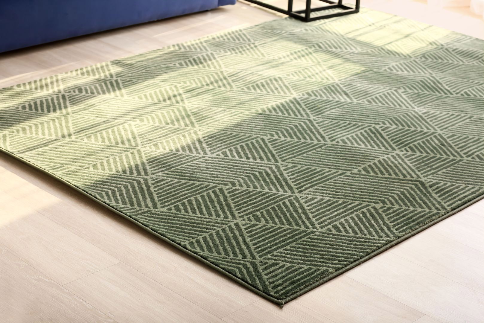 A green rug is sitting on a wooden floor in a living room next to a blue couch.