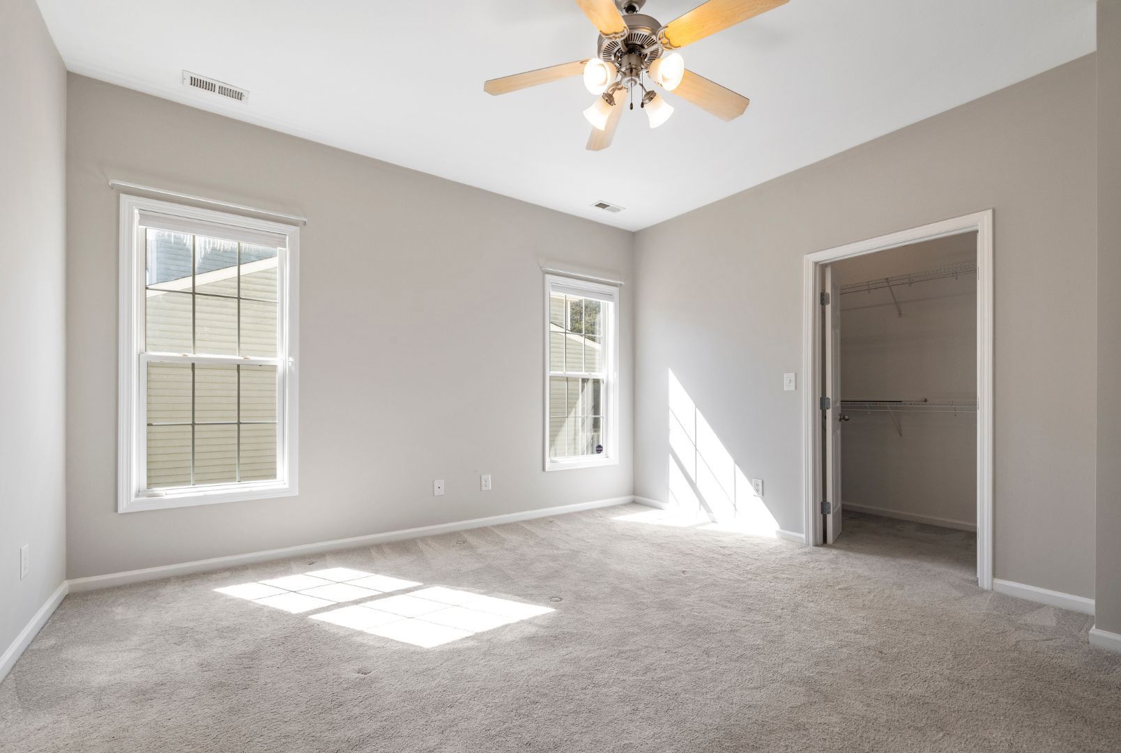 An empty bedroom with a ceiling fan and two windows.