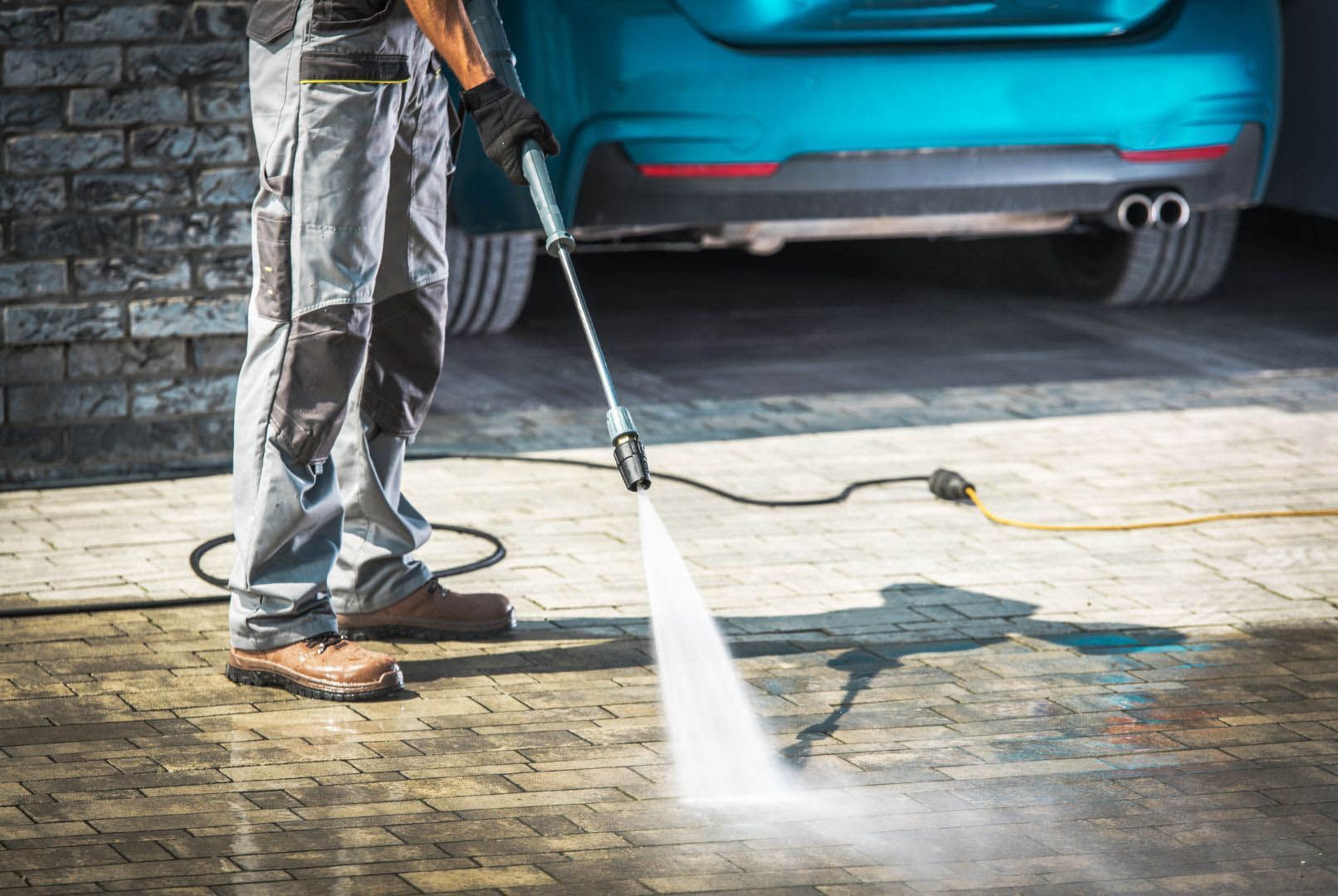 A man is using a high pressure washer to clean a driveway.