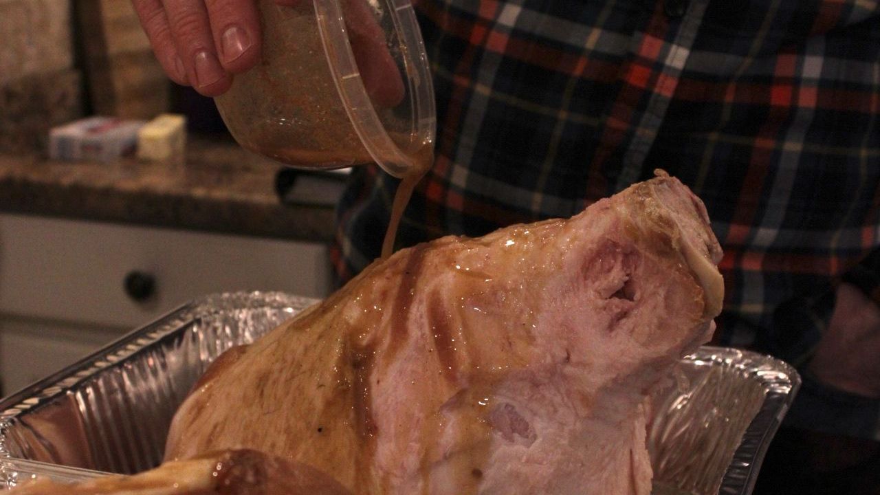 a person is pouring gravy over a pig 's head in a pan .