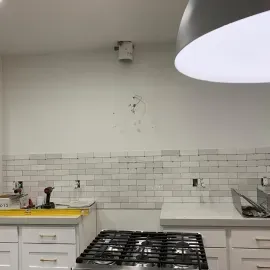 A kitchen with a white subway tile backsplash, a gas stovetop, white cabinets, and an unfinished wall with a pipe stub.