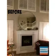 A room with a fireplace, a large round mirror above it, plantation shutters, and a 