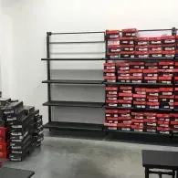 Shelving units in a storage area filled with stacked red and black shoe boxes, with several empty shelves to the left.