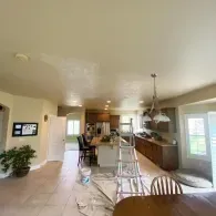 A kitchen interior undergoing painting, with a stepladder, drop cloths, and a ceiling showing patches of fresh white paint.