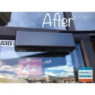 A dark-colored, rectangular hydraulic door closer mounted to the top frame of a glass door.