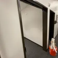 A view through a doorway into a room with white walls and gray carpet, with a red bucket of cleaning supplies nearby.