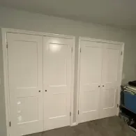 Two sets of white, dual-panel interior closet doors installed side-by-side on a gray wall above carpeted flooring.