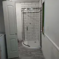 A walk-in shower with white subway tile walls and a glass door, situated next to a white door in a tiled room.