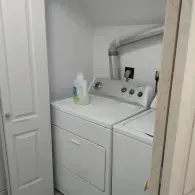 A white washer and dryer in a small, white closet, with a detergent bottle sitting on top of the washer.