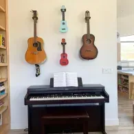 A digital piano with open sheet music sits below a wall display of two acoustic guitars and two colorful ukuleles.