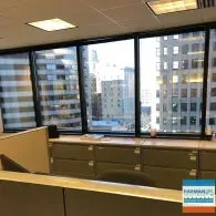A cubicle office space with large windows overlooking a city skyline and tall office buildings.