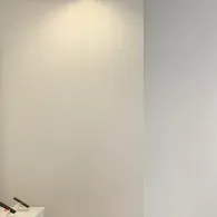 A plain white wall illuminated by a soft overhead light, with small product display stands visible in the lower corner.