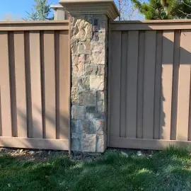 A stone pillar separates two brown wooden fence panels in a sunny outdoor setting.