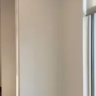 A smooth, off-white wall meets a white door frame on the left and a window frame with a light-colored blind on the right.