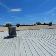 A view of a metal roof with several rectangular HVAC units against a blue sky with faint mountains in the distance.