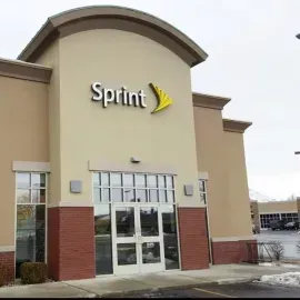 A beige and brick building storefront with a Sprint logo and yellow stylized wing symbol above the glass entrance doors.