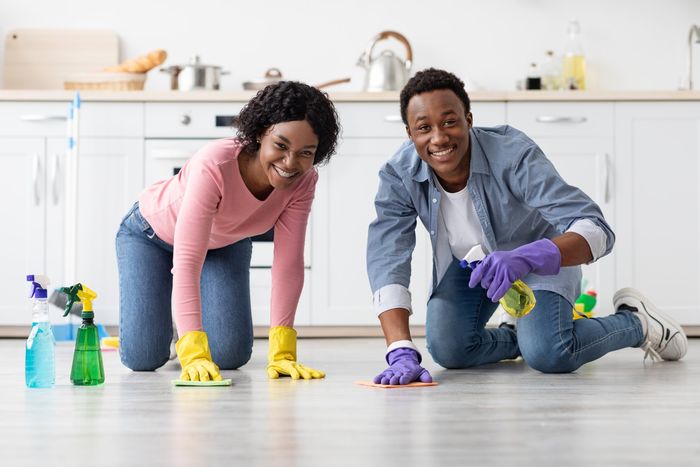 Happy african american couple in colorful gloves cleaning floor together in kitchen, using cloth and cleaning sprays.