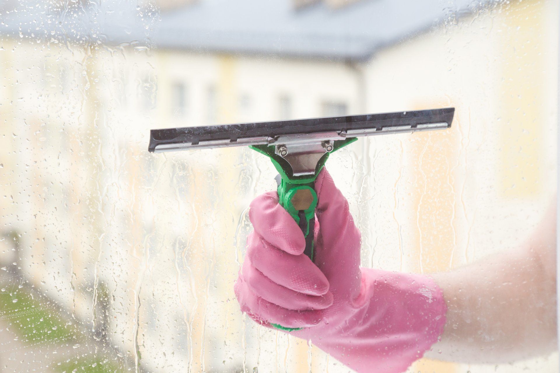 Cleaner's employee hand in pink protective glove washing and cleaning window