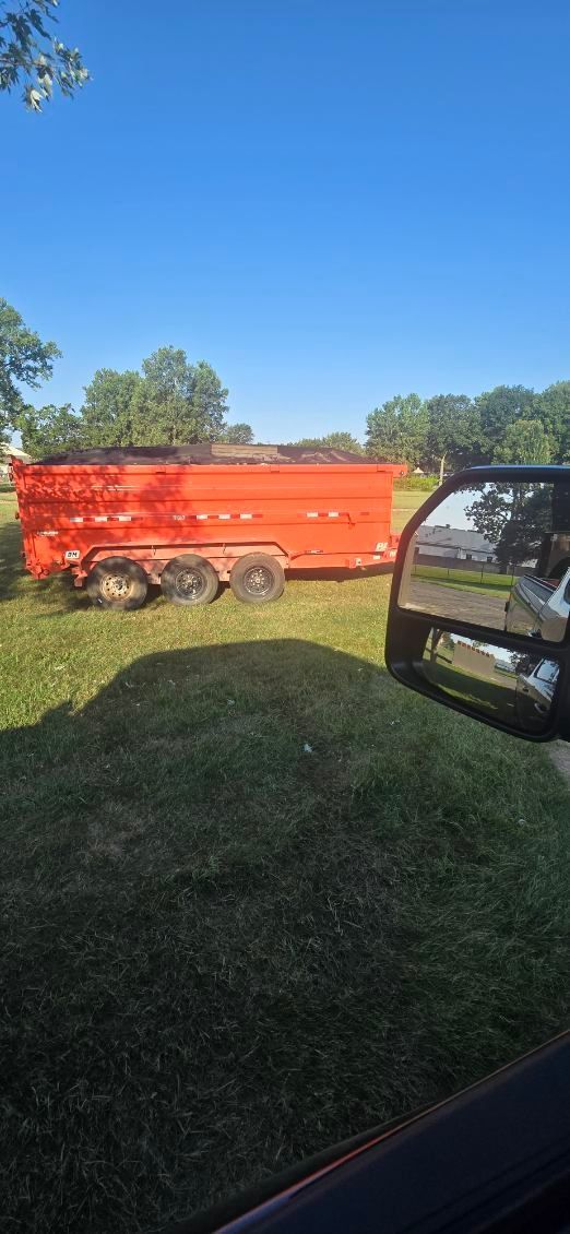 A red trailer on grass under a clear blue sky. A vehicle's side mirror is visible on the right.