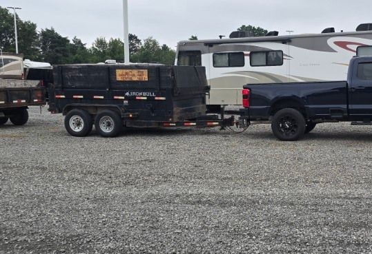 A dark blue truck pulling a trailer with a dumpster, parked on gravel.