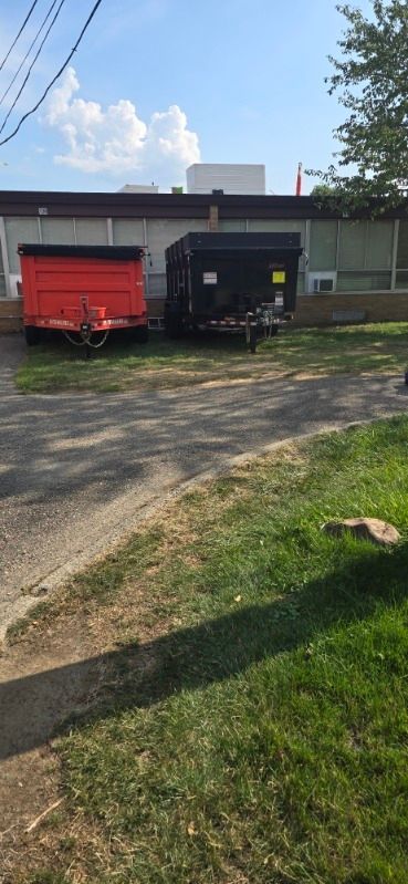 Two trailers, one red and one black, sit outside a building with a flag under a blue sky.