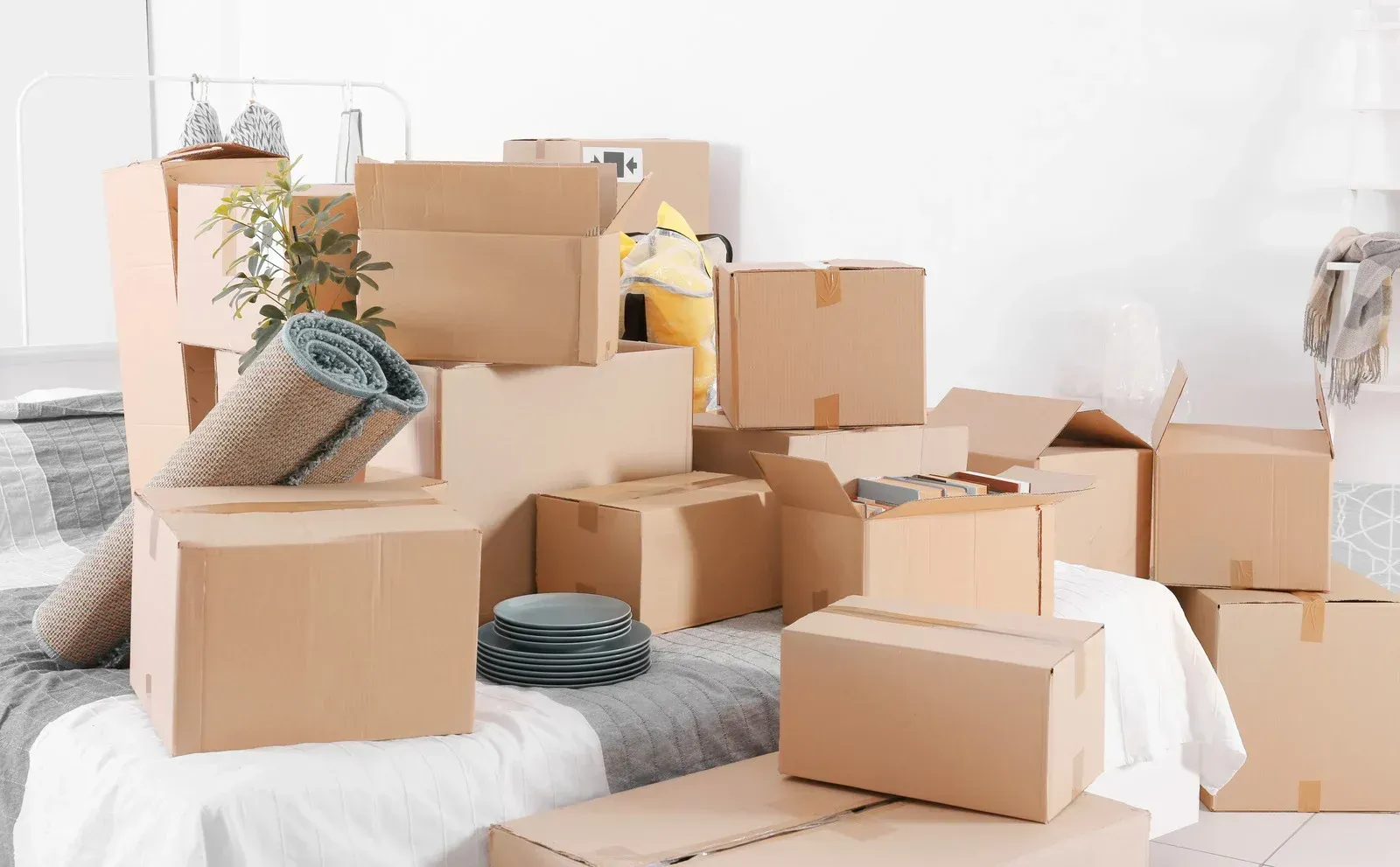 Boxes stacked on a bed, implying a move. Includes a rolled rug, dishes, and other items.