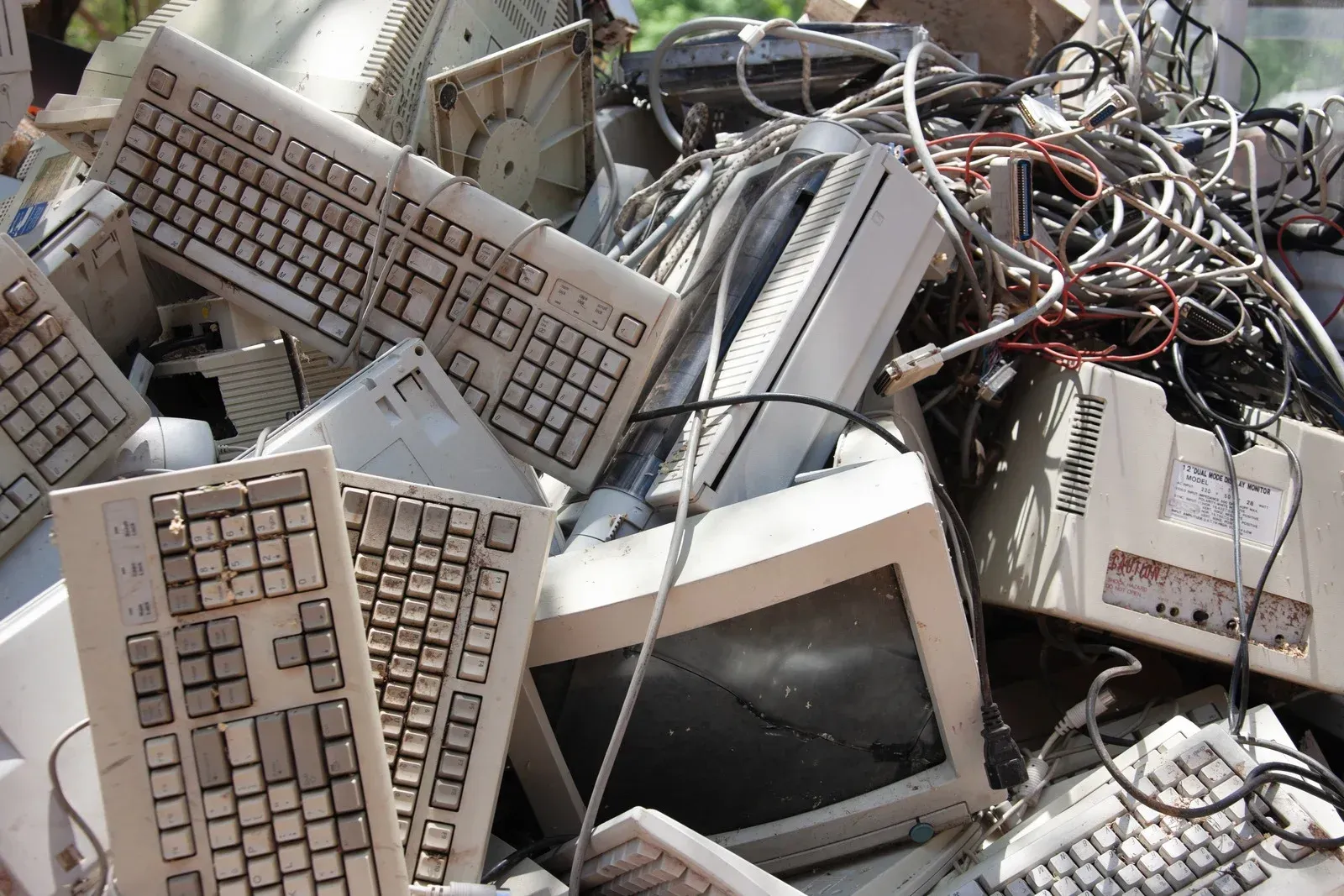 Pile of discarded beige computer equipment including keyboards and monitors.