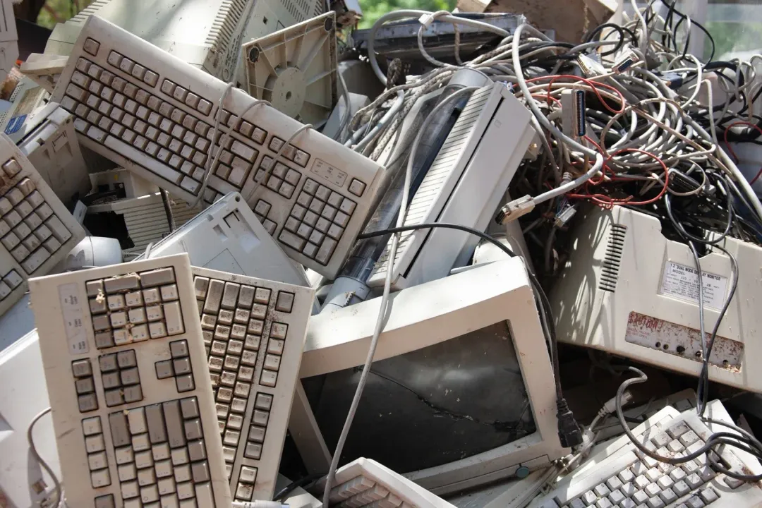 Pile of discarded beige computer equipment including keyboards and monitors.