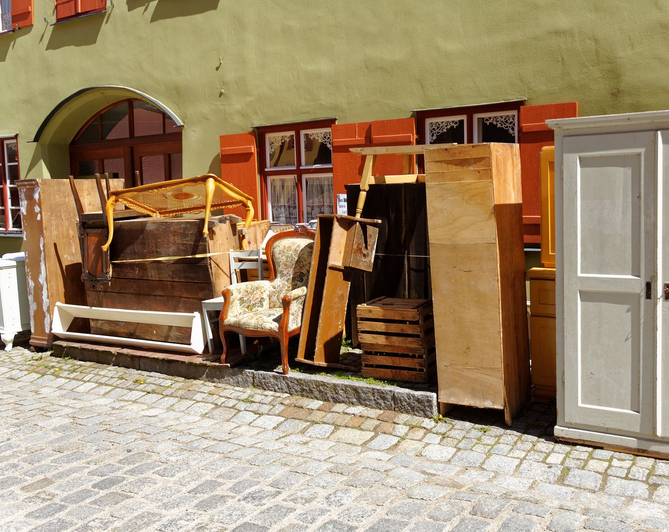 Pile of discarded furniture on a cobblestone street in front of a building.