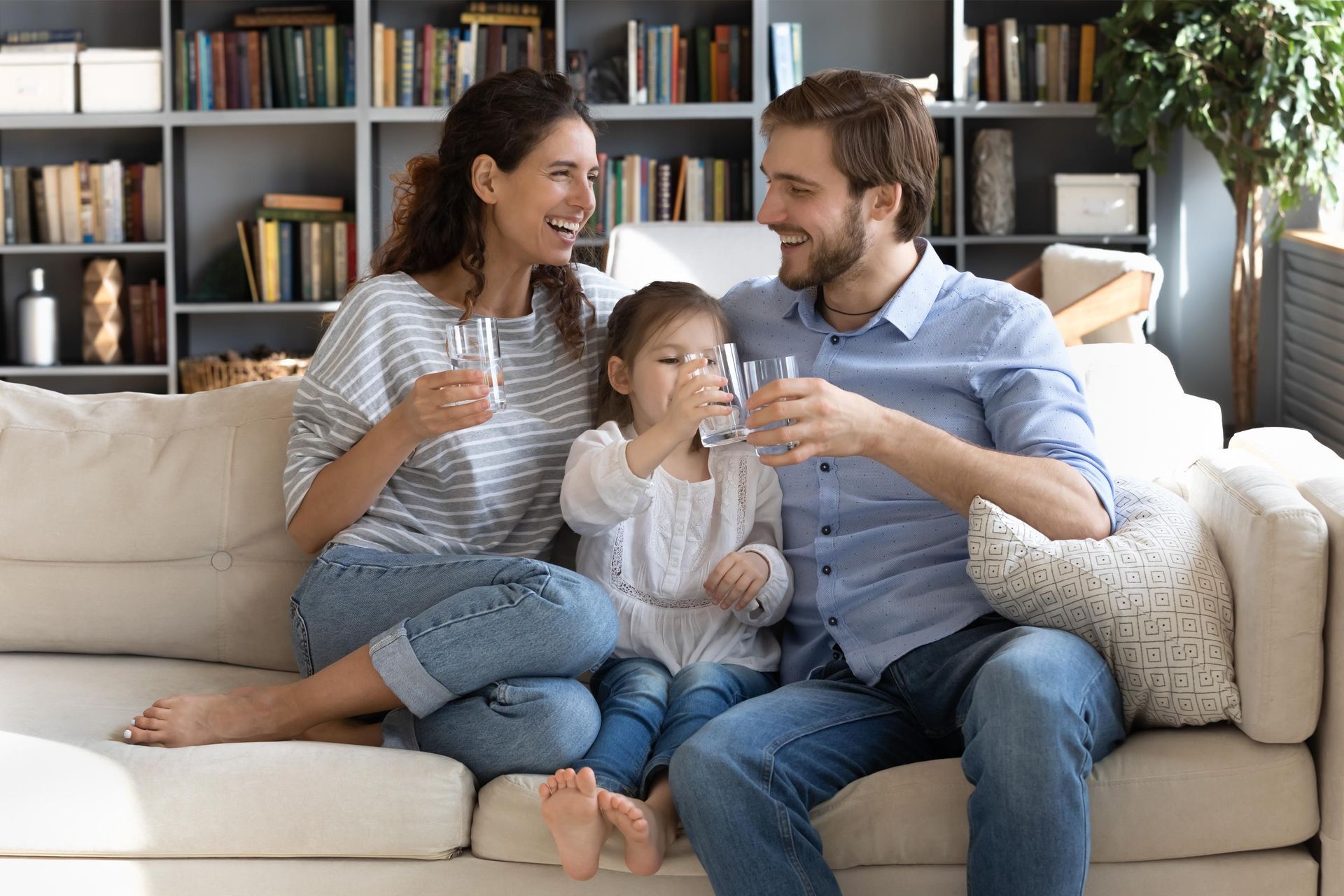 A family is sitting on a couch drinking water from glasses.
