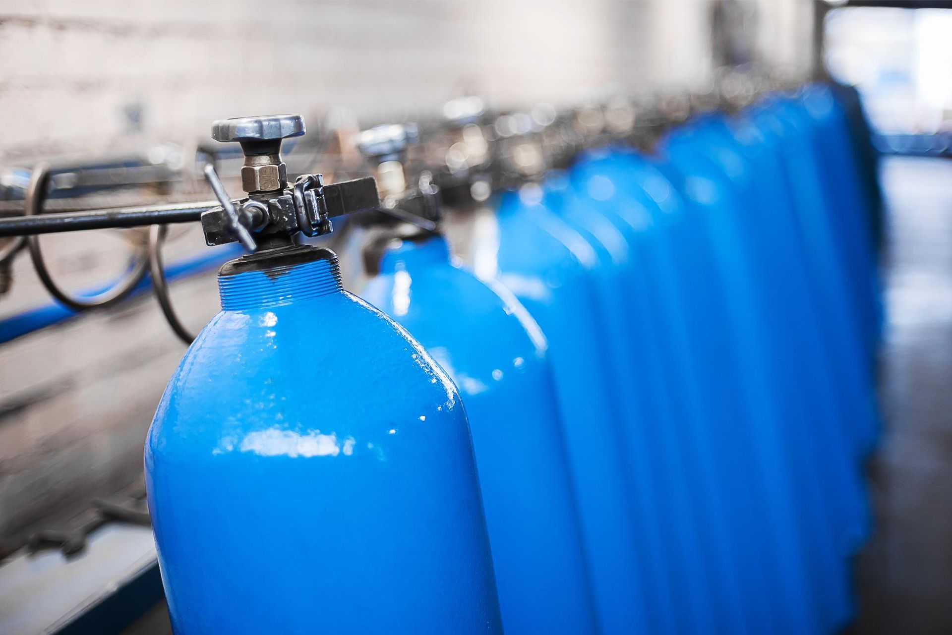 A row of blue gas cylinders are lined up in a factory.