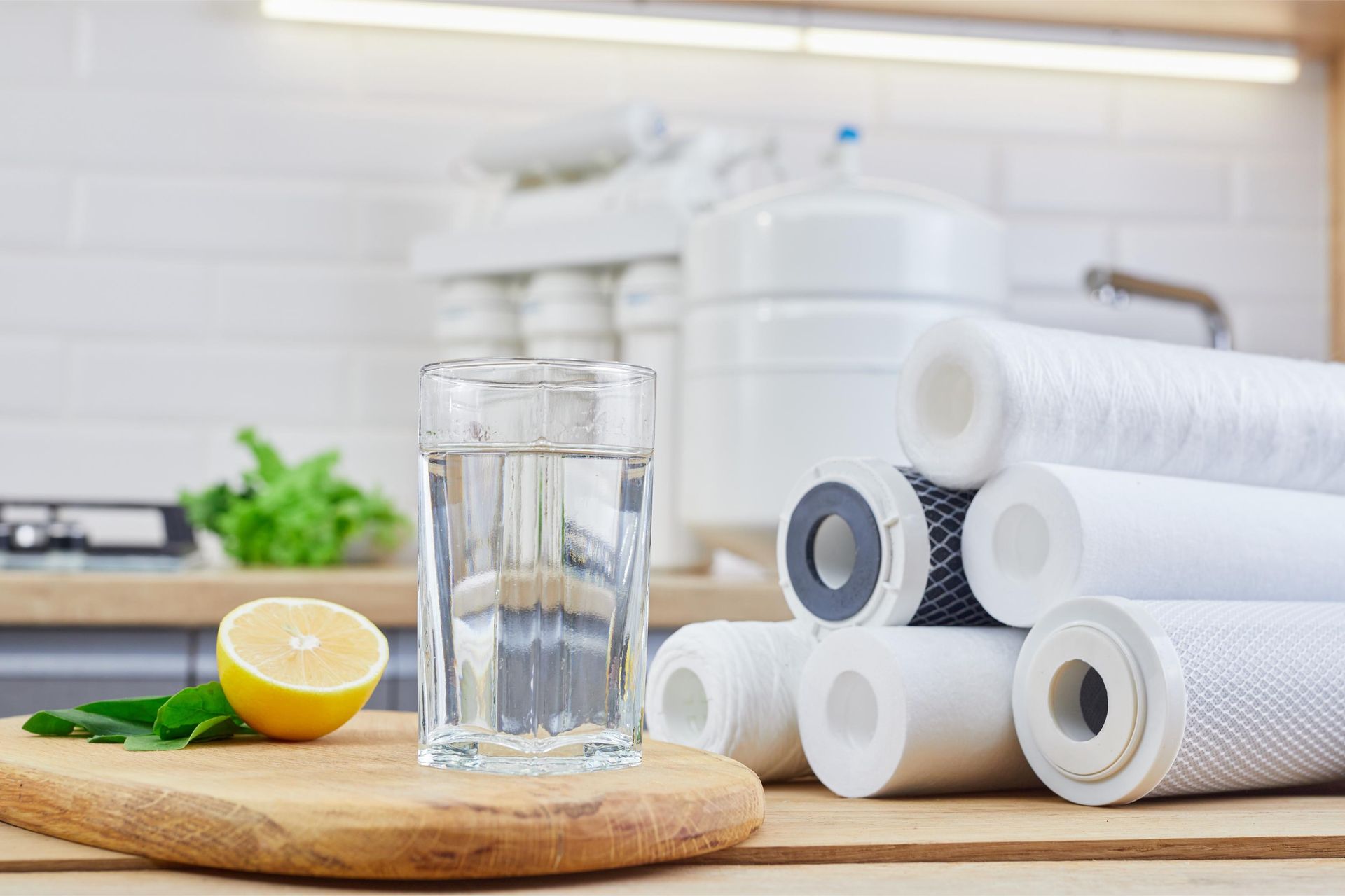 A glass of water , a lemon , and a stack of water filters on a cutting board.