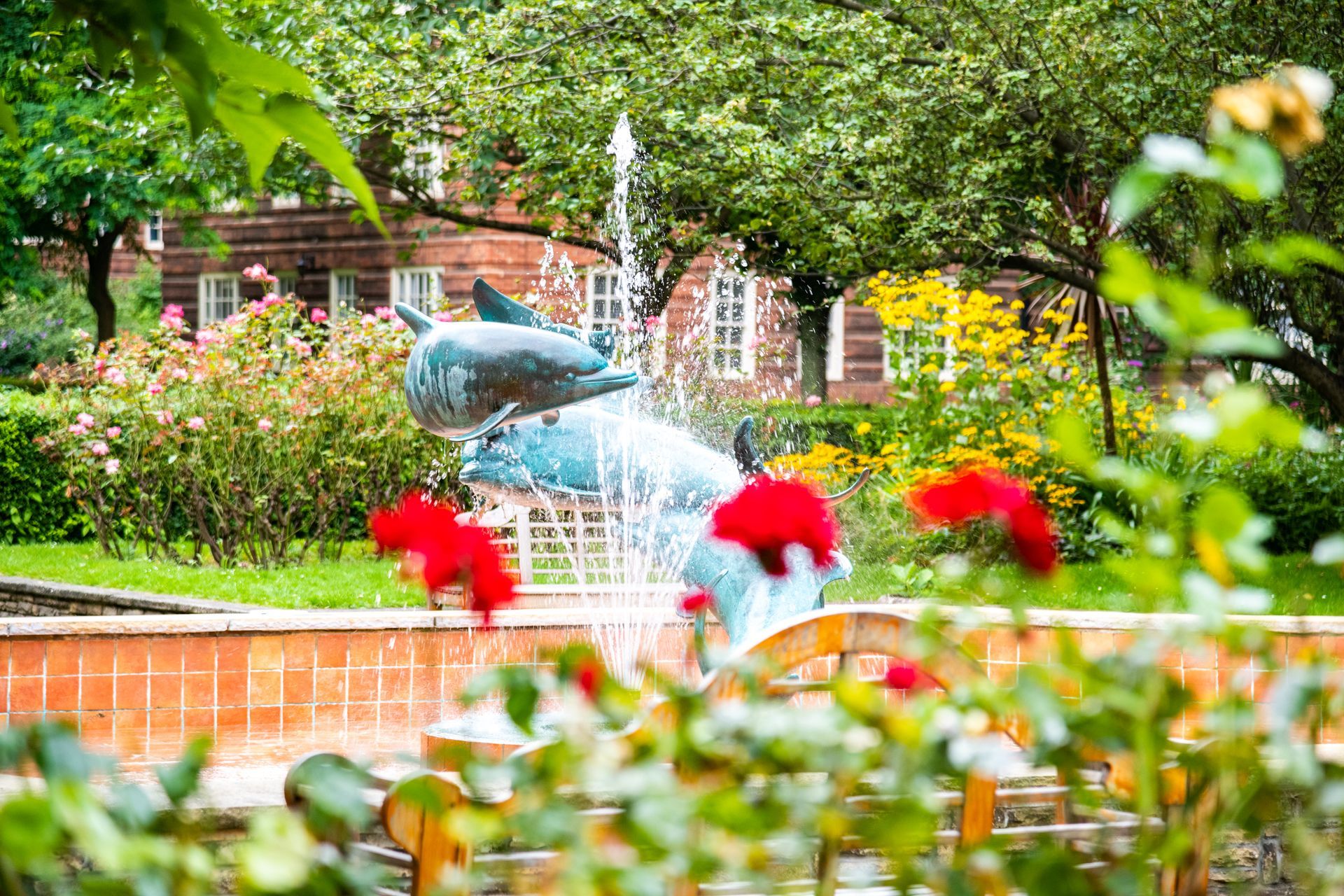 A fountain in a park with a statue of a dolphin in the background.