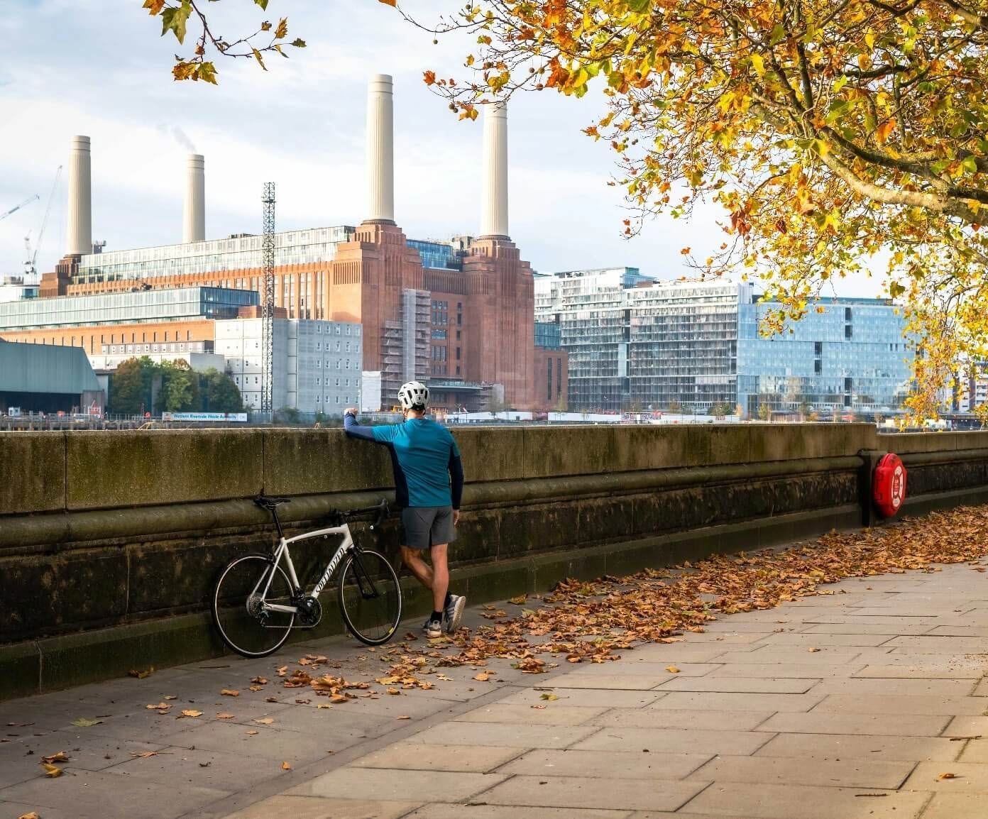 A man leaning on a wall next to a bicycle and looking over the river and the view of the city.