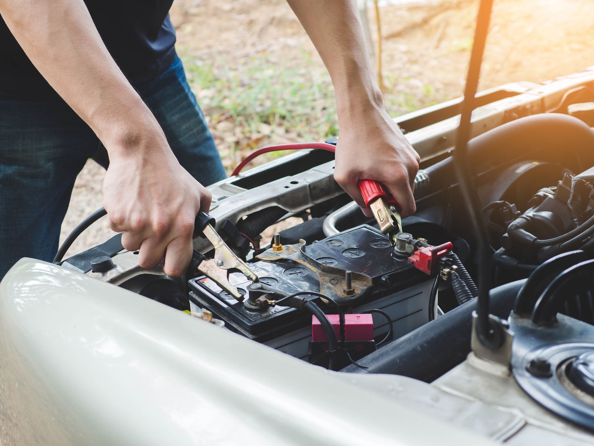 Person connecting jumper cables to a car battery under the open hood.