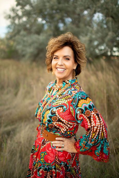 A woman in a red dress is standing in a field with her hands on her hips.