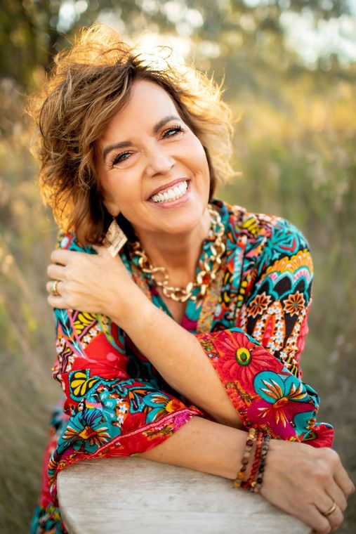 A woman is sitting on a bench with her arms around her shoulder and smiling.