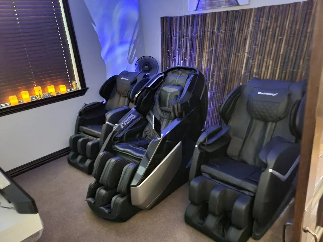 Three massage chairs are lined up in a room next to a window.